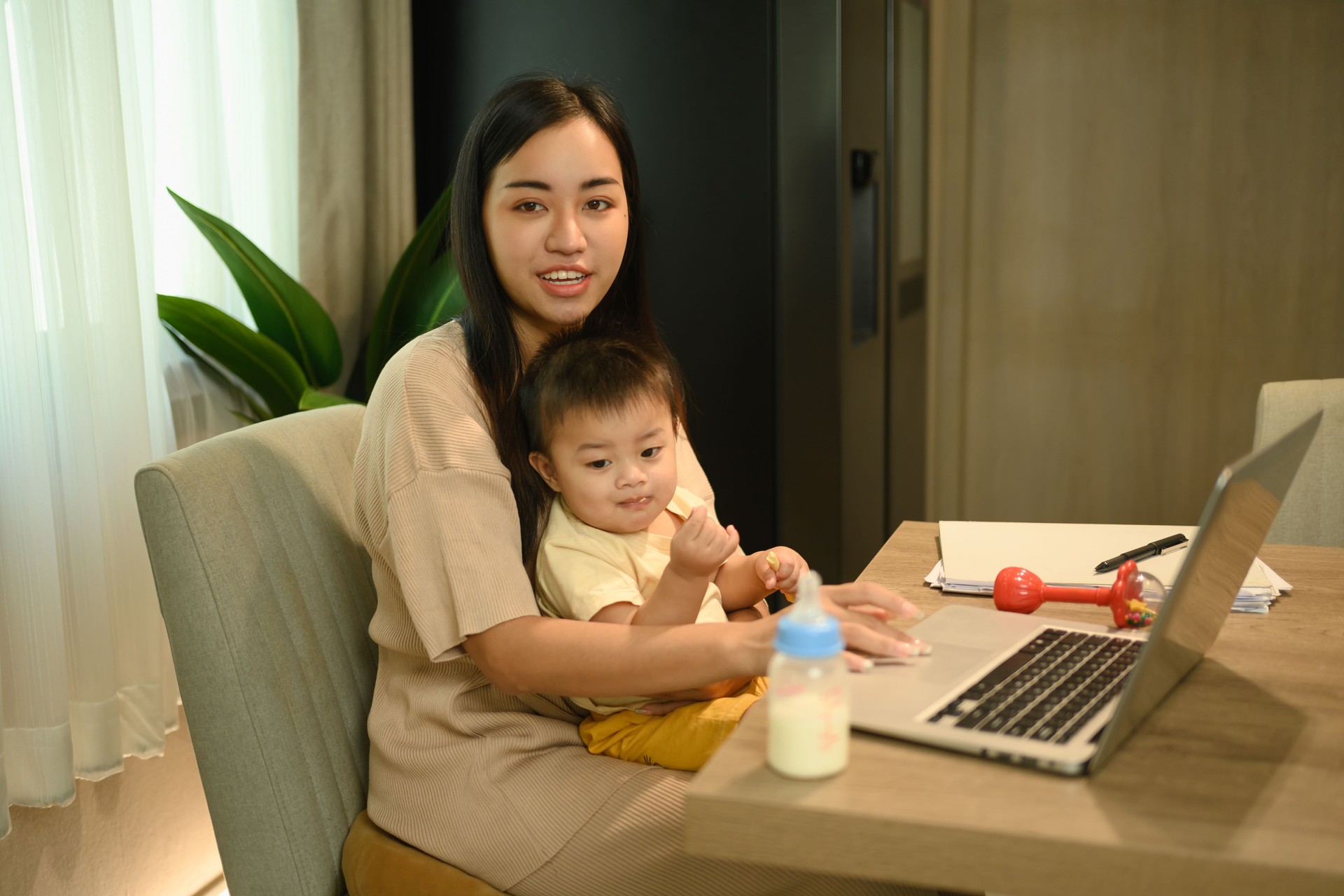 Loving young mother working remotely on laptop while taking care of her baby