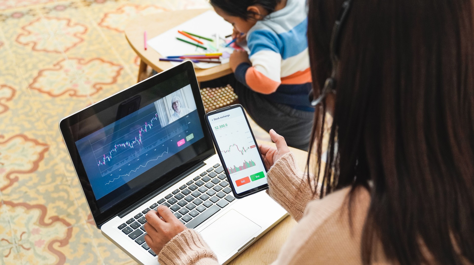 Asian trader mother studying stock market with child at home - Finance charts, future investment concept - Focus on mobile phone